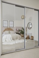 Master bedroom showing a mirrored wardrobe with a reflection of the double bed, pale pink panelling and soft furnishings.  