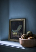 Bowl of fruit and painting next to blue painted wall on shelf