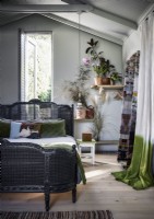 Grey rattan bed in country bedroom filled with houseplants
