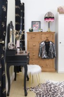 White furry covered stool and an upcycled decorative dressing table painted in black with a vinyl leopard print covered top in front of a pine chest of drawers