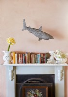 Floating shark sculpture above books on mantelpiece of fireplace