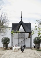 Ornate black chicken coop in white courtyard with hens