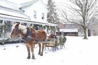 Vintage Amish farmhouse in the snow with mother and children in sleigh pulled by a Belgian horse.
