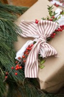 Close up of Christmas gift wrapped in brown paper decorated with ribbon, greenery and berries
