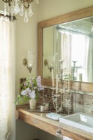 Elegant, feminine bathroom with vintage mirror, wood vanity and chandelier.