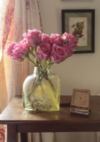 A vintage bottle makes a fitting vessel for roses in a hue in keepsing with the pink accents of the bedroom .