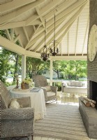 Deep overhangs give this shady porch the nostalgic feel of a classic barn. To balance the high ceilings and tall brick fireplace, Kathy chose high- backed wicker chairs that wouldnâ€™t look wimpy in the strong space. 