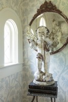 The foyer is home to an antique French cherub, a vintage mirror and metal table. The delicate blue and white wallpaper heralds the color palette of the interior of the home.