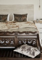 Carved wooden bench at foot of bed covered in fabrics 