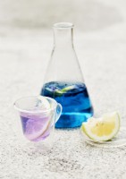 Coloured water in jug and class with slice of lemon in drink