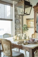 A massive bronze lantern hangs above breakfast room table. Built-in plate racks stretch from floor to ceiling to hold Anitaâ€™s collection of plates.