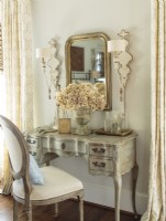 Artfully refinished by Anita, a curvy vanity shares center stage with a Louis Philippe mirror and wooden wall sconces outlined in gold paint.