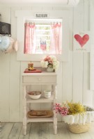 In the window, tea towels are clipped onto a curtain rod. A former nightstand find a new purpose for storing and displaying favorite items n the kitchen.