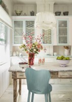 The glass doors of the original cabinets are tacked with lacy panels for a feminine look that also hides clutter. Painted a metallic blue, a kitchen chair becomes an eye-catching focal point. 