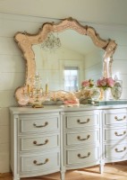 An antique Murano glass mirror presides over a French chest of drawer painted a soft grey.