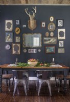 An accent wall painted a deep grey designates a dining area in the open space while providing a dramatic showcase for assorted family heirlooms and a vintage deer mount