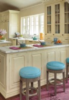 In the kitchen, electric-blue ottoman- style stools welcome guests to lounge at the counter. Neutral cabinetry, original to the house, makes a seamless backdrop for touches of color to pop ouT.