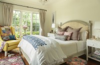 In the master bedroom, a graceful arched raffia-upholstered headboard frames a collection of striped and lattice-look pillows. A fringed, patterned rug brings art underfoot.