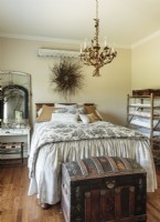 A gilded tole chandelier and bed outfitted with black-and- white ticking and toile impart a French- countryside sensibility to the guest bedroom.
