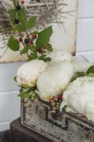 A small vintage chest function as a container for a fresh arrangement of fluffy peonies and berry-laden branches.