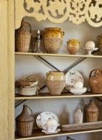 The antique cabinet holds an assortment of wicker-wrapped jugs, olive oil jars and vintage dishes.

