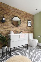 White sink cabinet with drawers and toilet against an exposed brick wall in in a modern bathroom 