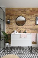 White sink cabinet with drawers against an exposed brick wall in in a modern bathroom 