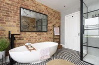 Monochrome modern bathroom with a crittall shower enclosure and an eggshell shaped ceramic bathtub against an exposed brick wall 
