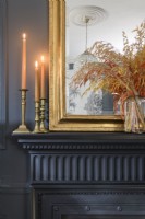 Detail of lit candles and candlesticks and gold framed mirror on a Victorian black painted mantlepiece