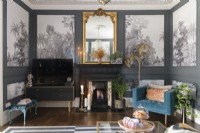 Black painted Victorian fireplace with gold mantle mirror in a grey painted living room with paneling filled with monochrome tropical tree wallpaper