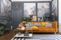 Orange velvet sofa in a grey living room with panels infilled with monochrome tropical tree patterned wallpaper
