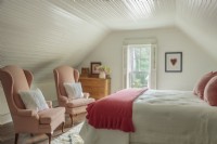 Original beadboard walls and ceiling and under the eaves architecture confer a cocoon-like feel to the  bedroom.