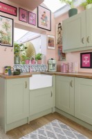 White butlers sink in the corner of a colourful pale pink and green Shaker retro style kitchen with an open hatch through to a conservatory
