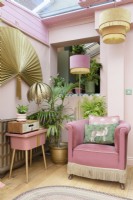 Small pale pink coloured conservatory with open hatch though to kitchen with a reclaimed vintage armchair