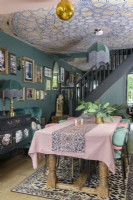 Open plan dark green dining area with mosaic wallpapered ceiling and tassle fringed art deco style lamps