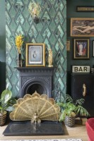 Black Victorian fireplace with art deco green patterned wallpaper and gold peacock fan decorative fireguard