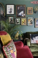 Salon style gallery wall in a green living room with red and green velvet sofas.