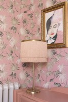 Fringed art deco style table lamp on a reclaimed chest of drawers in front of palm leaf patterned wallpaper