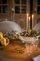 Candles lit in bowl of decorative foliage on dining table