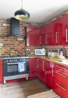 Exposed brickwork wall and red cabinets in modern kitchen