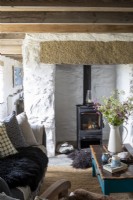 Living room with white washed walls, wooden beams and comfortable furniture.  Large vase of wild flowers picked from the surrounding countryside, and wood burner behind.