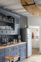 Sally and John Biddle's house in Cornwall, Blue painted kitchen cupboards, and modern Smeg fridge, with surfboard attached to ceiling beams