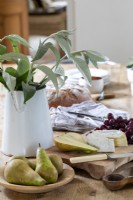 Kitchen table detail, with foliage in vase, mixed cheeses, pears, and grapes