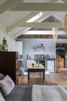 Converted barn, with view through to simple kitchen and wooden farmhouse table. Wooden beams and rustic decoration.