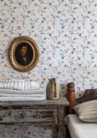 Gilded framed portrait on floral wallpapered wall in vintage bedroom