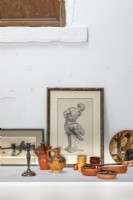 Detail of ceramics and framed paintings on white wall shelf
