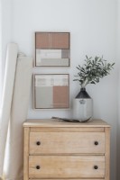 Framed fabric artworks above stripped wooden chest of drawers