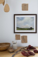 Framed landscape painting above desk with autumnal branches 