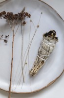 Sage bundle for burning and dried flowers on white plate - detail
