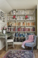 Wall of bookshelves in small reading room with desk and armchair